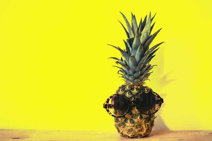 green pineapple fruit with brown framed sunglasses beside yellow surface