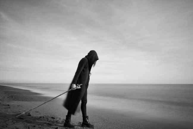 woman in black cloak with fishing pole standing in beach